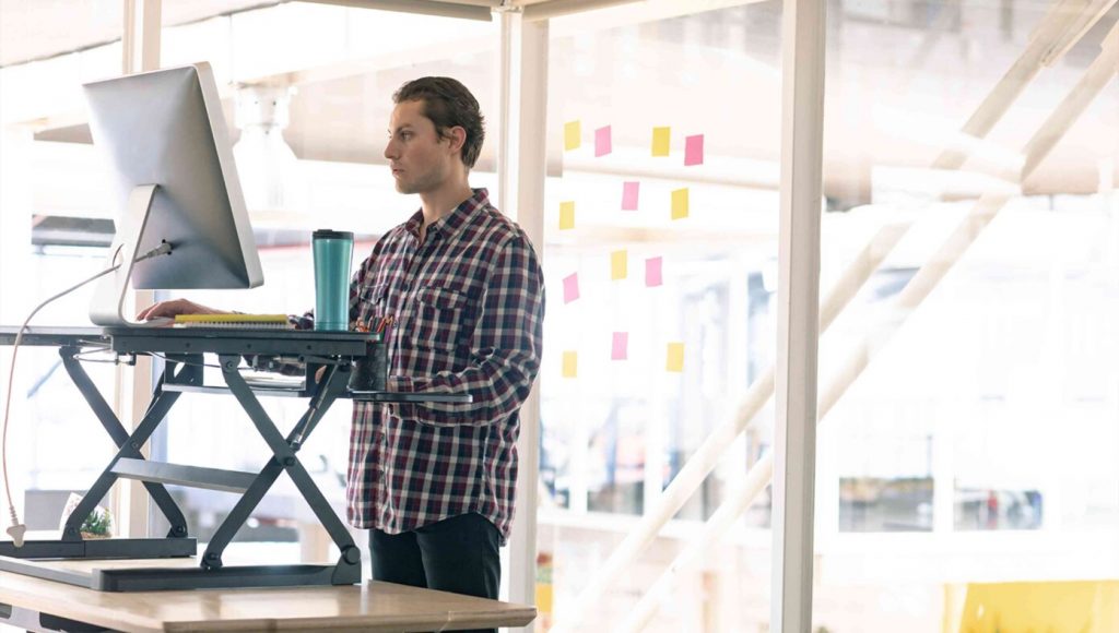 SATIRE – Coworker Standing At Desk Obviously Just Hasn’t Learned About Chairs Yet